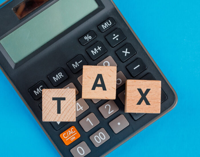 Tax planning concept with wooden cubes on calculator on blue background flat lay.